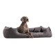 Ein brauner Hund sitzt bequem auf einem plüschigen schwarzen Haustierbett in einem modernen Raum mit weißen Wänden und dekorativen Elementen.