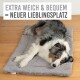 Ein entspannter Australian Shepherd liegt auf einem weichen grauen Haustierbett, mit dem Text "EXTRA WEICH & BEQUEM = NEUER LIEBLINGSPLATZ" darüber.