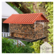 Ein Vogelhaus in Form eines Hauses mit einem roten Ziegeldach, gefüllt mit verschiedenen Samen, hängt von einem Baumzweig.