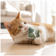 Chat roux et blanc allongé sur le sol tenant et mordillant un jouet en tissu à motif de feuilles vertes.