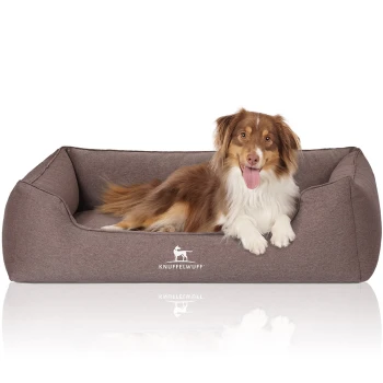 Ein braunes Hundebett mit plüschigem Design, auf dem ein Hund bequem ruht. Das Bett hat das Logo "KNUFFELWUFFF" deutlich sichtbar.