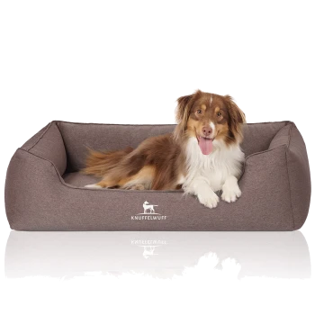 Ein braunes Hundebett mit plüschigem Design, auf dem ein Hund bequem ruht. Das Bett hat das Logo "KNUFFELWUFFF" deutlich sichtbar.