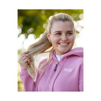 Eine Person trägt einen rosa Hoodie mit dem Aufdruck 'SPOOKS EQUESTRIAN' und hält ihre langen Haare im Freien.