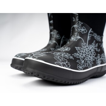 Nahaufnahme von stilvollen schwarzen Gummistiefeln mit weißen Blumenmustern und einem weißen Rand, geeignet für nasses Wetter.