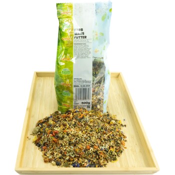 Ein 500g Beutel mit buntem "Farb Maus Futter" für Mäuse steht auf einem Holztablett, mit etwas Futter, das davor verschüttet ist.