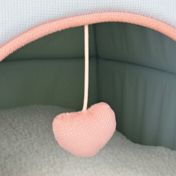 Ein gemütliches Haustierbett-Interieur mit einer weichen, plüschigen weißen Basis und einem hängenden, herzförmigen Spielzeug in Pink.