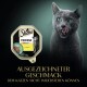 Eine graue Katze, die sich die Lippen leckt, neben einer Sheba Finesse Katzenfutterverpackung, mit "mit Huhn" und dem Satz "AUSGEZEICHNETER GESCHMACK."