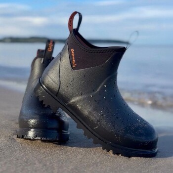 Schwarze wasserdichte Knöchelstiefel mit Profilsohlen und Wassertropfen am Strand; Anhänger mit der Aufschrift 'Gateway Jo'.
