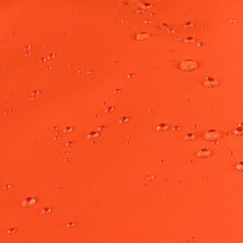 Nahaufnahme eines orangefarbenen wasserdichten Stoffes mit kleinen Wassertröpfchen, die über die Oberfläche verteilt sind.