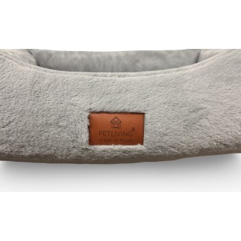 Graues samtiges Haustierbett mit braunem Lederetikett mit der Aufschrift 'PETLIVING place to enjoy' und Pfote-im-Haus-Logo.