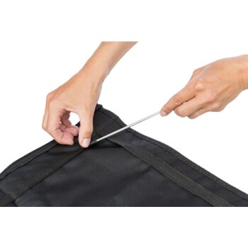 Eine Person, die eine schwarze Haustierbox zusammenbaut, indem sie einen Metallstab in die Stoffkante einfügt, um den Aufbauprozess zu demonstrieren.