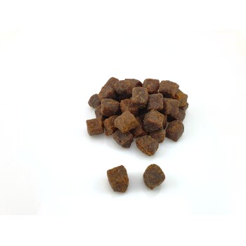 Une pile de petites friandises pour animaux de compagnie de couleur marron foncé en forme de cubes, sur un fond blanc.