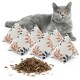 Eine graue Katze mit leuchtend orangefarbenen Augen sitzt neben fünf dekorativen Katzenminzkissen mit Blattmustern und einem Haufen getrockneter Katzenminze.
