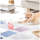 Eine verspielte hellorange Katze, die nach einem rosa interaktiven Spielzeugball auf einem bunten Teppich in einem gemütlichen Wohnzimmer greift.