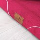 Eine Nahaufnahme eines lebhaften rosa Haustierbettes mit einem braunen Lederetikett, das den Markennamen "tierlando" auf einem hellen Holzboden zeigt.