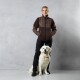 Eine Person in einer braunen Fleecejacke und schwarzen Hosen steht neben einem lächelnden Golden Retriever vor einem grauen Hintergrund.