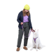 Eine Person in einer marineblauen Jacke, lila Hemd und gelber Mütze steht mit einem weißen Hund an einer lila Leine, beide lächeln.
