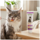 Gray long-haired cat licking food from a spoon beside a tube labeled "Support Optimize & Care" pet paste on a table.