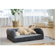 Flauschiger sandbraun-weißer Hund liegt auf einem grauen Bolster-Hundebett mit kleinem Lederetikett in einem hellen Wohnzimmer.