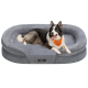 Ein glücklicher schwarz-weißer Hund mit einem orangefarbenen Halstuch liegt auf einem plüschigen grauen Hundebett mit erhöhten Rändern.