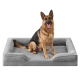 Deutscher Schäferhund sitzt auf einem grauen, plüschigen, rechteckigen orthopädischen Hundebett mit erhöhten Seitenpolstern und U-förmig abgesenkter Vorderseite.