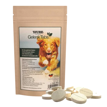 Ein Paket von TJURE Gelenk Tabs für Hunde, das eine braune Papiertüte mit einem grünen Etikett zeigt, umgeben von mehreren runden Tabletten.