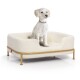 Ein flauschiger weißer Hund sitzt bequem auf einem stilvollen, cremefarbenen Haustierbett mit einem goldenen Metallrahmen.