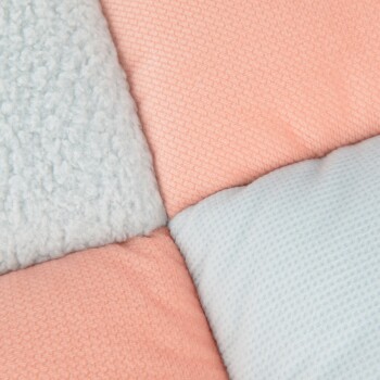 Eine Nahaufnahme einer weichen Haustierdecke mit einem Patchwork-Design in pastellrosa und blauen Farben, mit unterschiedlichen Texturen.
