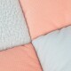 Eine Nahaufnahme einer weichen Haustierdecke mit einem Patchwork-Design in pastellrosa und blauen Farben, mit unterschiedlichen Texturen.
