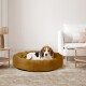 Ein gemütliches, rundes Hundebett in warmem Braun mit einem kleinen Hund, der bequem darin ruht, in einem modernen Wohnzimmer.