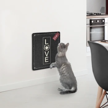 Eine graue Katze steht auf ihren Hinterbeinen und greift nach einem schwarzen, an der Wand montierten Kratzbrett, auf dem das Wort 'LIEBE' gedruckt ist.