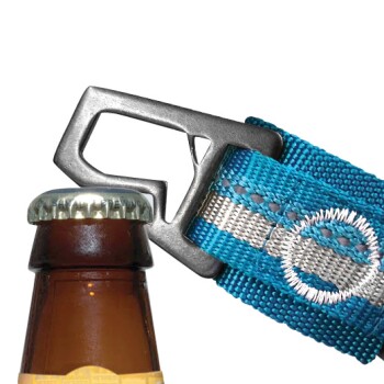 Nahaufnahme einer braunen Bierflasche mit einem silbernen Deckel, neben einem blau-grauen gewebten Gürtel mit einem Metallflaschenöffner.