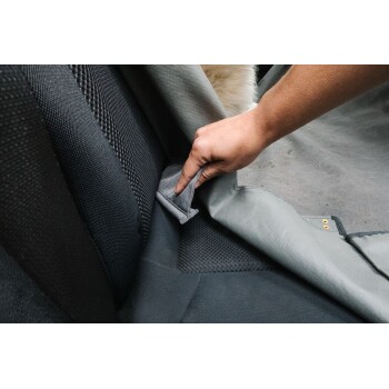 Eine Hand zieht eine graue Autositzabdeckung für Haustiere zurück und zeigt den schwarzen Stoff des darunterliegenden Sitzes.