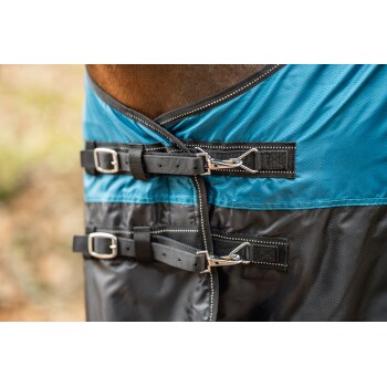 Nahaufnahme einer Pferde-Decke mit einem blauen oberen Abschnitt und einem schwarzen unteren Teil, gesichert mit verstellbaren Riemen und Schnallen.