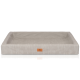 Ein plüschiges, rechteckiges Haustierbett in einer sanften beige Farbe mit erhöhten Kanten und einer lederähnlichen Textur, mit einem kleinen braunen Logoetikett.