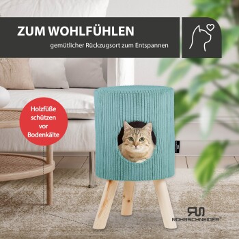 Ein türkisfarbenes Katzenversteck mit Holzbeinen und einer Katze, die durch eine kreisförmige Öffnung schaut. Text: "ZUM WOHLFÜHLEN" und "Holzfüße schützen vor Bodenkälte."