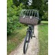 Ein Fahrrad mit einem großen Korb aus Weide, der einen Metallkäfig auf einem Weg umgeben von Grün zeigt.