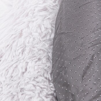 Eine Nahaufnahme eines Haustierbettes mit einer flauschigen weißen Seite und einer strukturierten grauen Seite mit kleinen Punkten, die das doppelte Design zeigt.