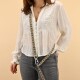 Eine Frau trägt eine weiße bestickte Bluse und graue Jeans und hält eine gemusterte Haustierleine. Der Hintergrund ist ein sanftes Beige.