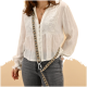 Eine Frau trägt eine weiße bestickte Bluse und graue Jeans und hält eine gemusterte Haustierleine. Der Hintergrund ist ein sanftes Beige.