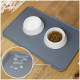 Eine graue Futtermatte für Haustiere mit zwei weißen Schalen, eine gefüllt mit Trockenfutter, und einer Nahaufnahme von verschütteten Wassertropfen auf der Matte.