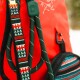 Nahaufnahme eines lebhaft roten Haustier-Rucksacks mit einem grünen gemusterten Gurt und einer bunten Seitentasche mit geometrischen Designs.