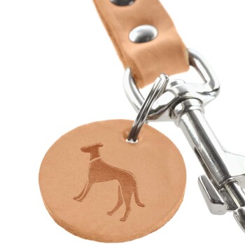 Eine Nahaufnahme eines hellbraunen Leder-Hundemarkenanhängers mit einer geprägten Silhouette eines Hundes, befestigt an einem silbernen Metallclip.