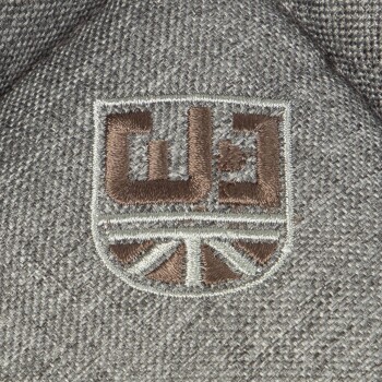 Grauer Stoff mit einem gestickten Logo mit den Buchstaben "C3" und einem stilisierten Union Jack-Design darunter.