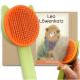 Eine bunte Katzenbürste mit einem orangefarbenen Kopf und einem grünen Griff, neben einer Cartoon-Löwenfigur auf einer Verpackung mit der Aufschrift "Leo Löwenkatz" und "Katzenbürste."