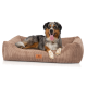Ein glücklicher Australian Shepherd Hund, der auf einem plüschigen, tanfarbenen Hundebett mit gerippter Textur liegt, mit einem Logo-Patch, das 'KNUFFERLUFF' liest.