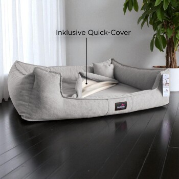 Graues rechteckiges Haustierbett mit erhöhten Seiten, weichen Kissen und inklusive Schnellbezug, auf dunklem Holzboden platziert.