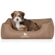Ein kleiner, flauschiger Hund sitzt bequem in einem braunen Haustierbett mit einem Logo, das "KNUFFELWUFF" liest. Das Bett hat ein weiches, strukturiertes Innere.
