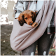 Eine Person in einer karierten Jacke hält einen kleinen Hund in einer weichen, beigen Haustiertragetasche, die eine gemütliche Transportoption für Haustiere zeigt.