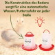 Rot-weiße GarPet-Kükenfutterspender auf Einstreu mit Küken im Hintergrund; sichtbarer Text: 'Wasser/Futterzufuhr'.